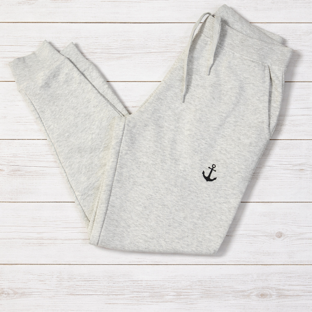 Gray sweatpants with an anchor emblem on a light wooden surface