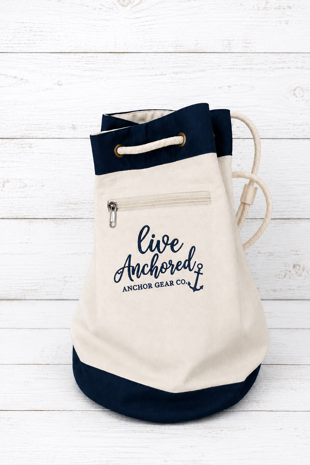 Canvas drawstring bag with navy accents and 'Live Anchored' text on a white wooden background