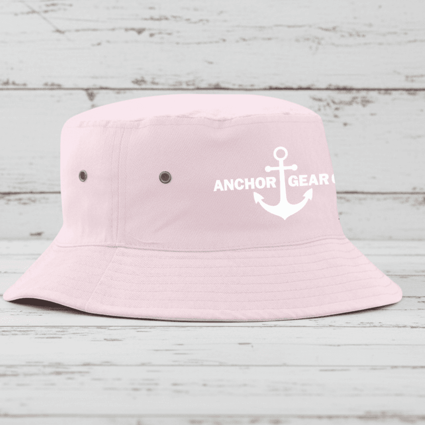 Pink bucket hat with 'Anchor Gear' logo on a wooden surface by a body of water.