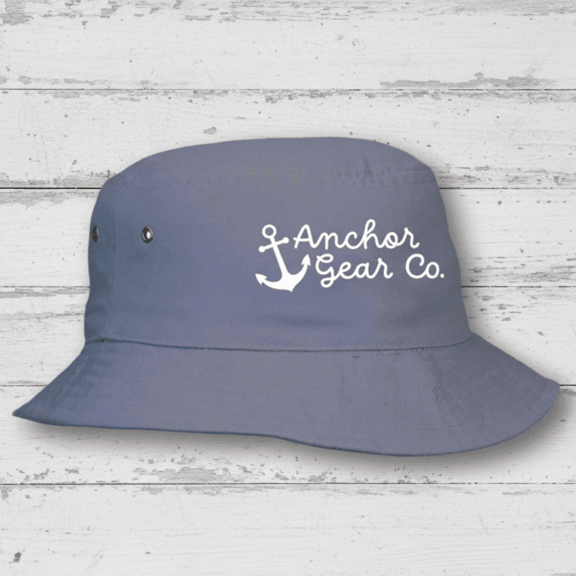 A blueberry coloured Youth Nautical Bucket Hat with a whimsical Anchor Gear Co. logo on the front, displayed on a wooden surface.