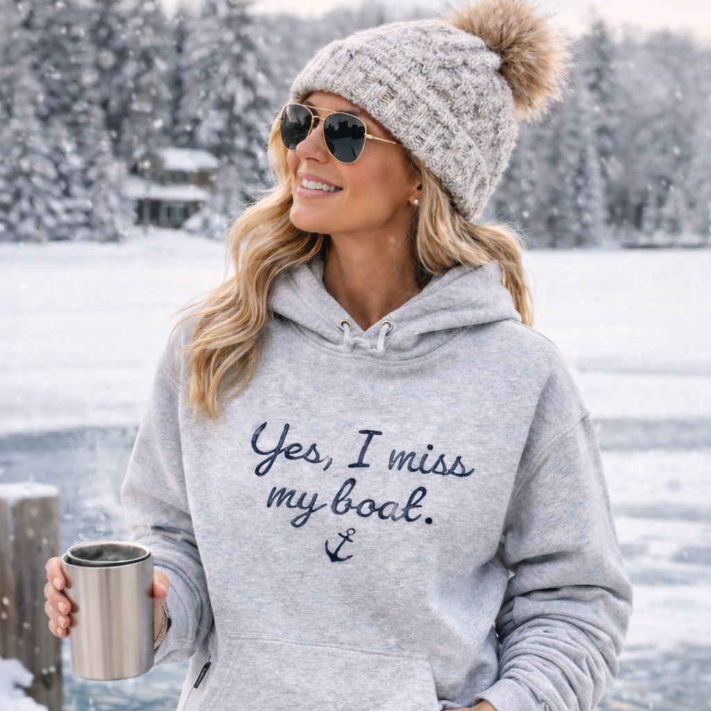 Woman in a gray hoodie with text, sunglasses, and knit hat standing in a snowy landscape.
