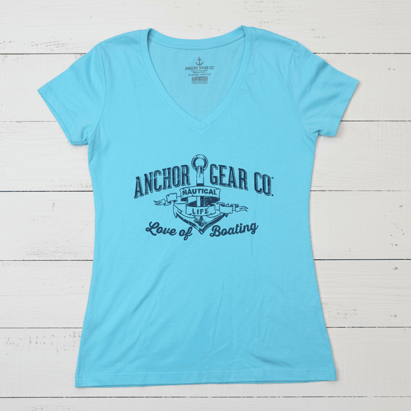 A teal blue fitted women's t-shirt with a v-neck, featuring a white graphic print of an anchor and text, displayed on a wooden surface.