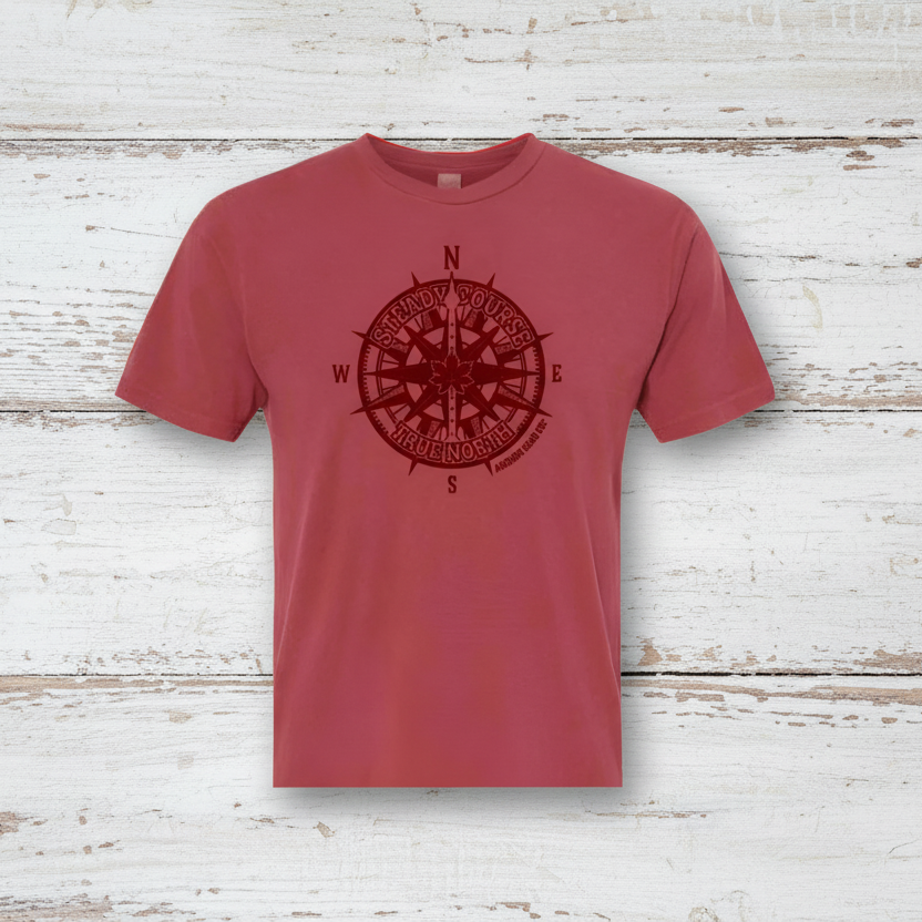 Red t-shirt with a compass design against a scenic background of trees and water.
