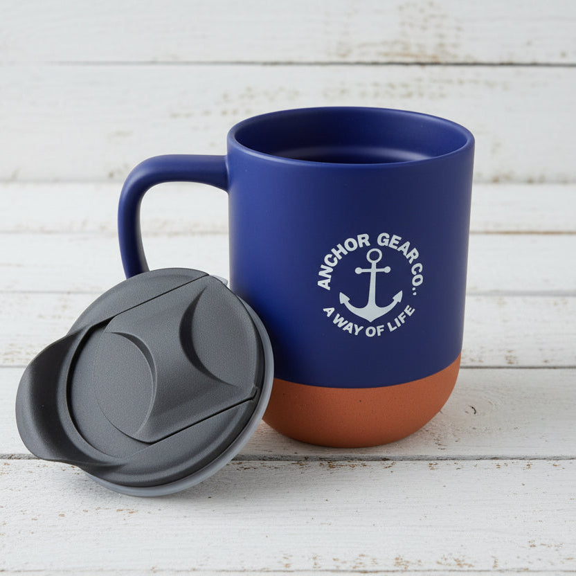 A navy-colored ceramic mug with a cork bottom and a black secure sip lid, featuring the Anchor Gear Co. logo.