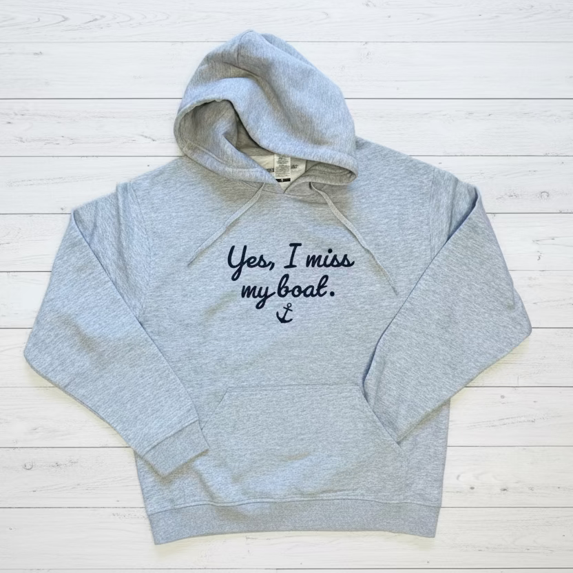 Gray hoodie with 'Yes, I miss my boat' text on a wooden floor