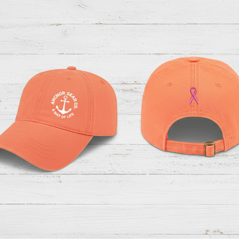 Two melon colour caps displaying the Anchor Gear logo and a cancer ribbon, one showing the front view and the other showing the back view with an adjustable strap.