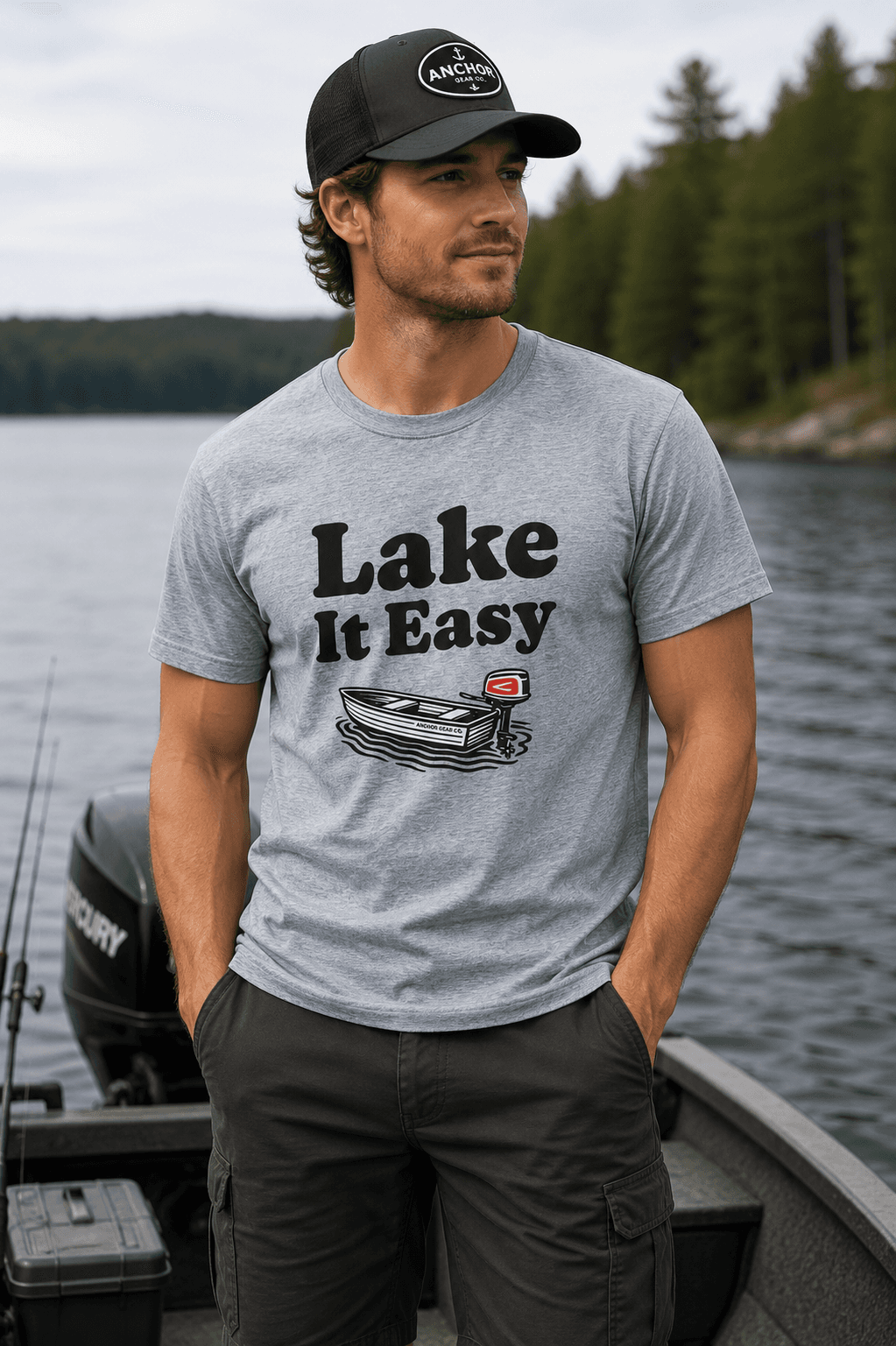 Man wearing the Lake It Easy graphic tee by Anchor Gear Co. standing on a boat with a lake and forest in the background