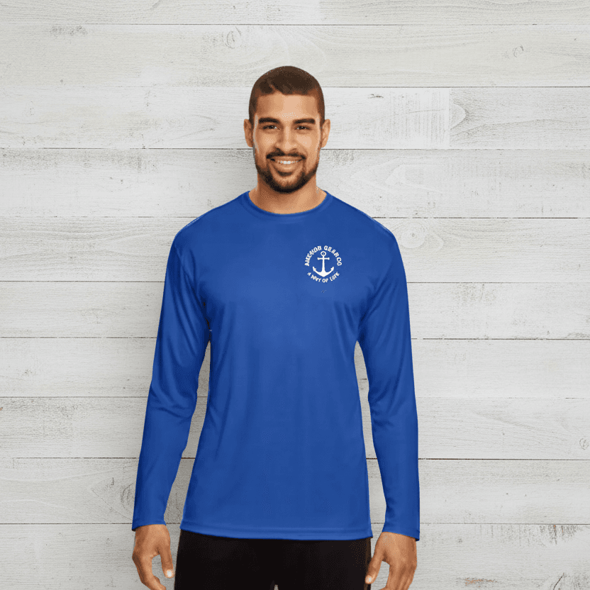 A man standing by a body of water wearing a blue long sleeve UV shirt with a white anchor logo on the chest.