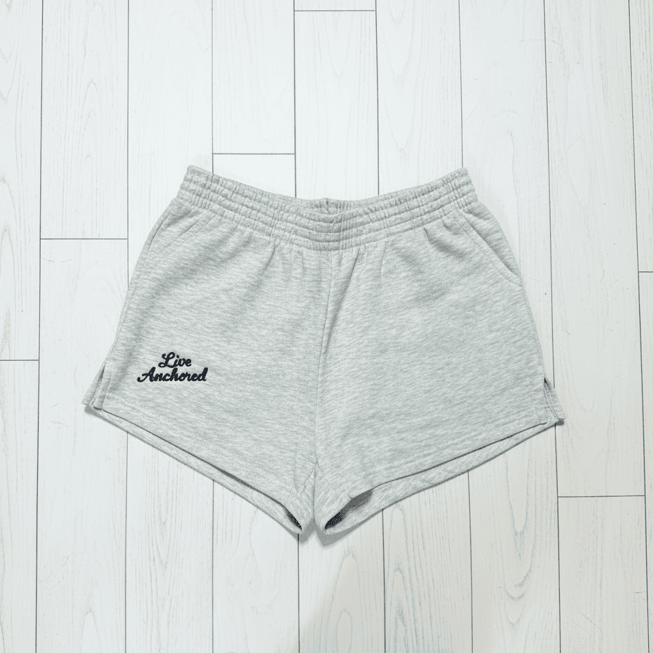 Gray shorts with 'Live Anchored' text on a light wooden floor