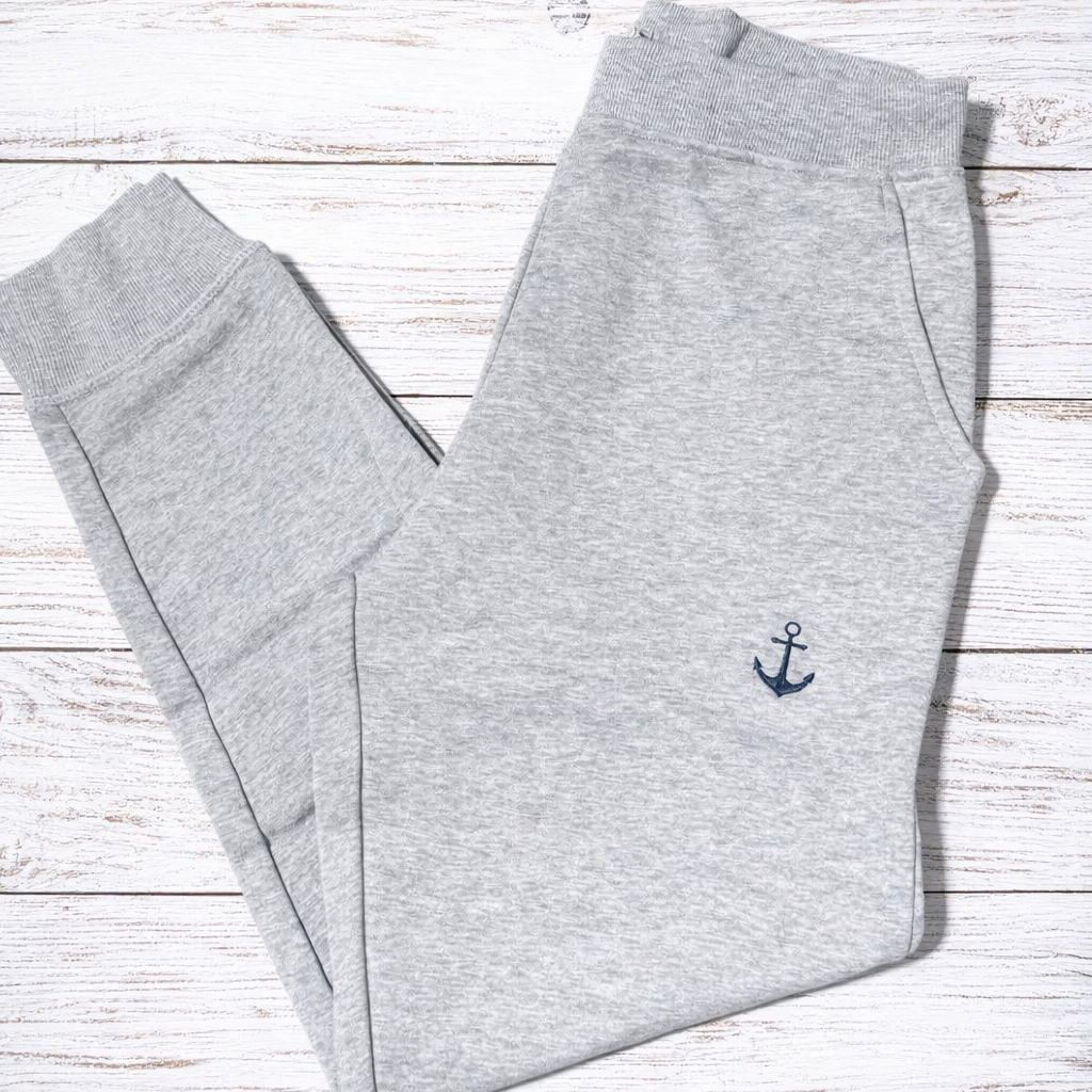 Gray sweatpants with an anchor emblem on a wooden surface