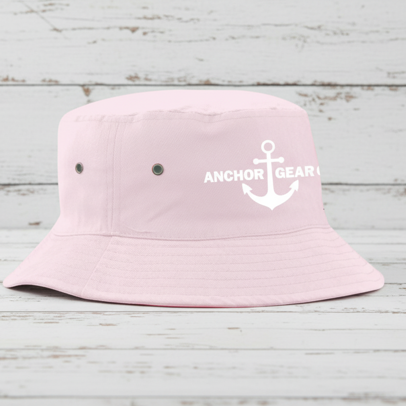 Pink bucket hat with 'Anchor Gear' logo on a wooden surface by a body of water.