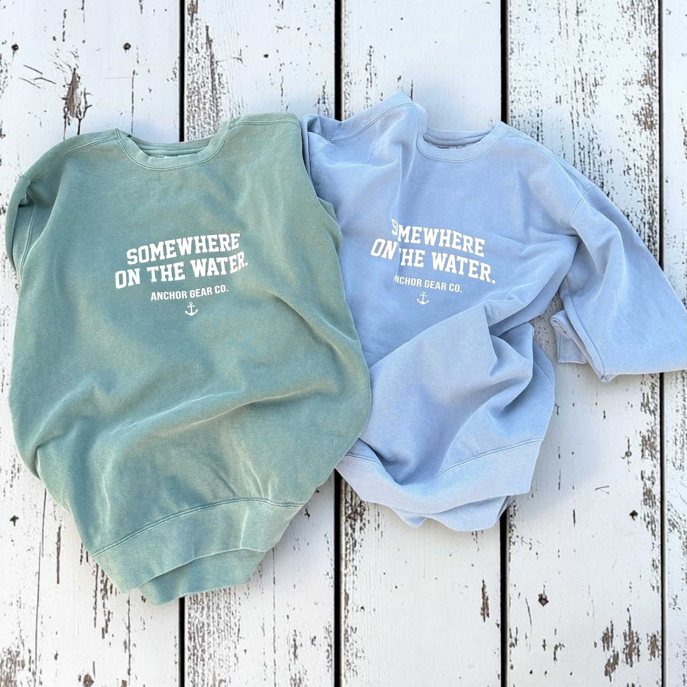 Two sweatshirts, one green and one blue, with text on a wooden surface.