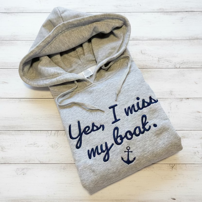 Folded hoodie with 'Yes, I miss my boat' text on a wooden floor