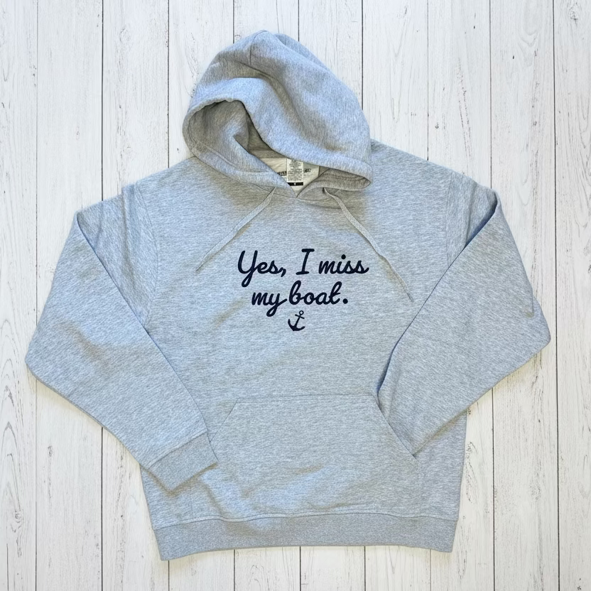 Gray hoodie with 'Yes, I miss my boat' text on a wooden floor