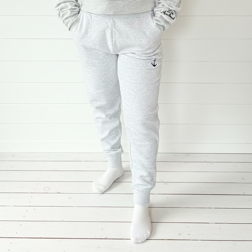 Person wearing a gray tracksuit standing in a room with wooden walls and a colorful rug.