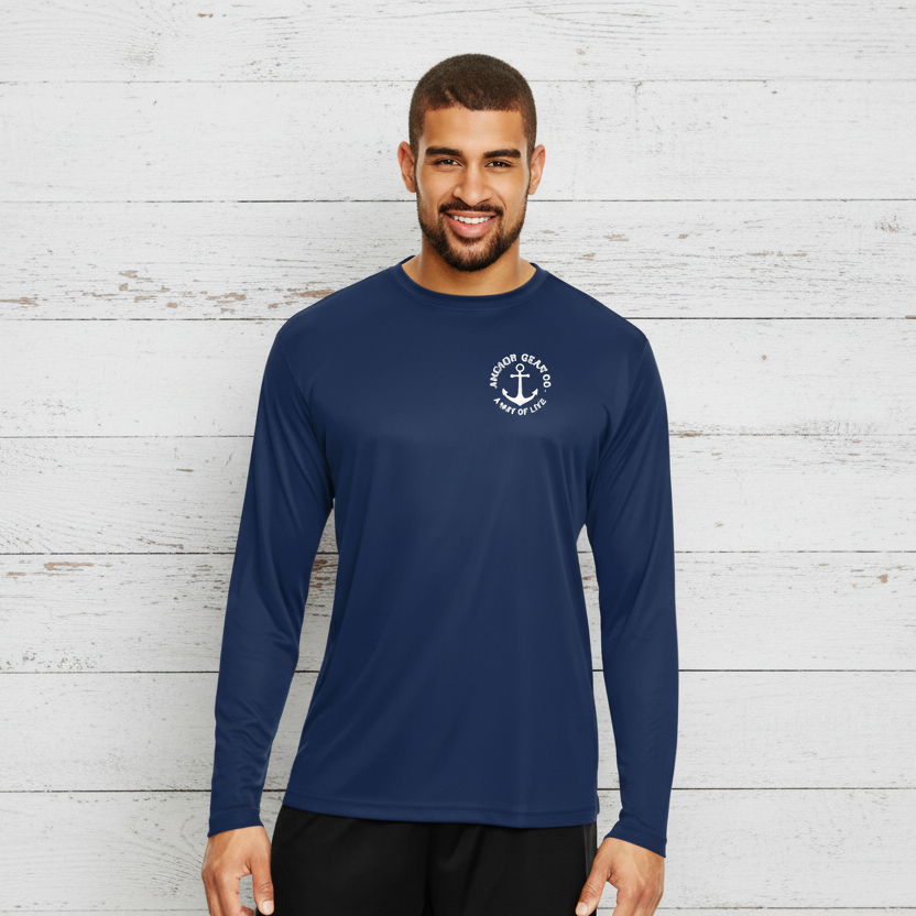 A man standing by a body of water wearing a blue long sleeve UV shirt with a white anchor logo on the chest.