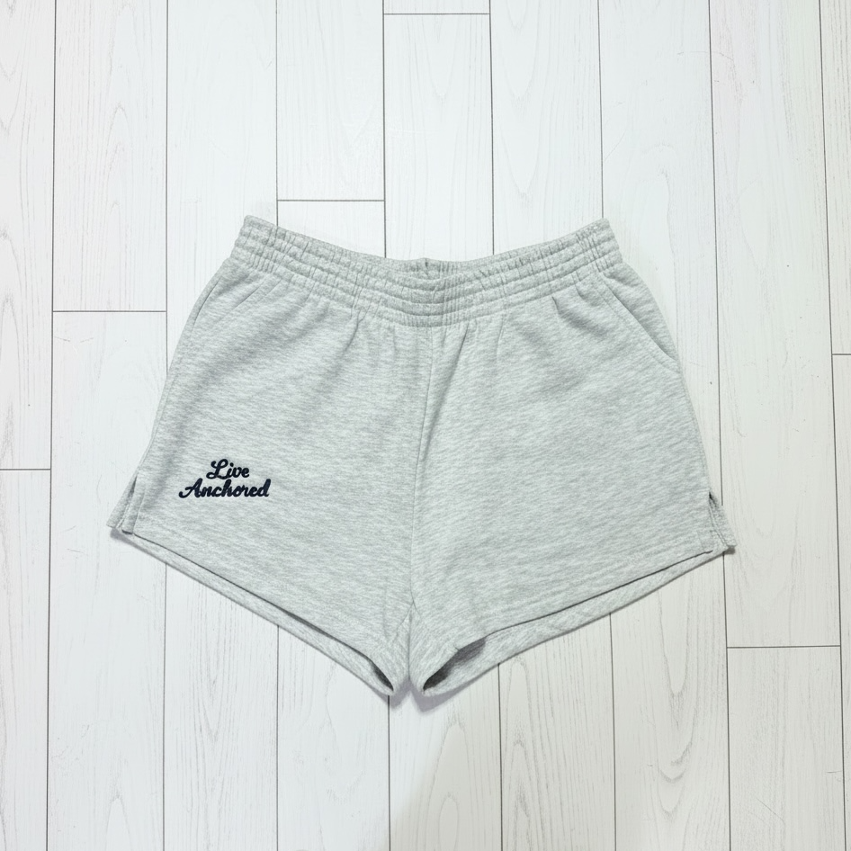 Gray shorts with 'Live Anchored' text on a light wooden floor