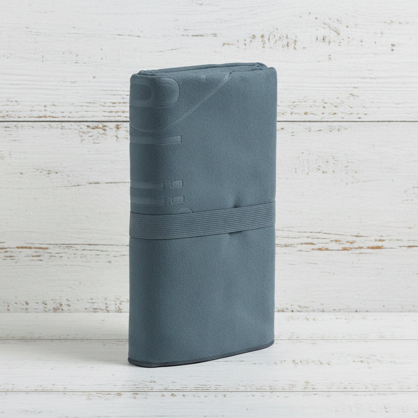 A charcoal Talii Towel draped over a flat surface with a person standing in front, holding the towel at the top, showing the size and colour of the towel.