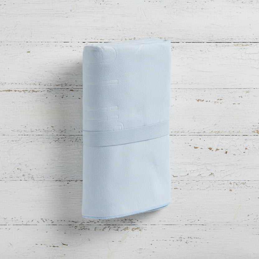 A ice blue Talii Towel draped over a flat surface with a person standing in front, holding the towel at the top, showing the size and colour of the towel.