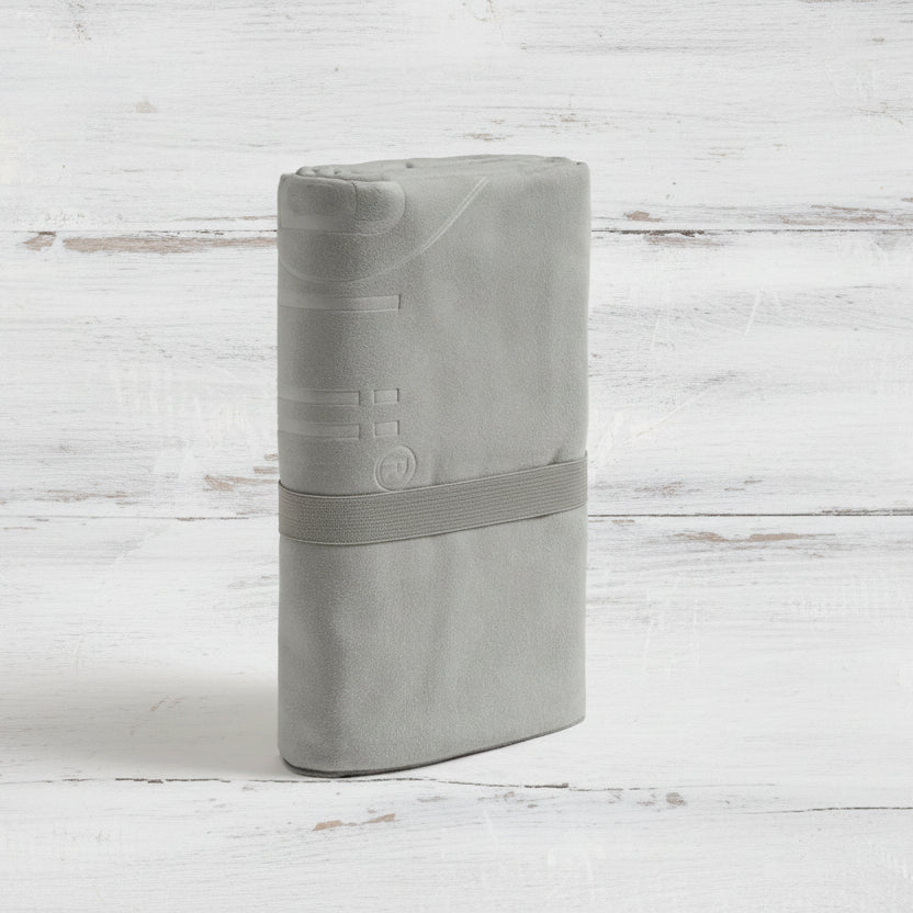 A light grey Talii Towel draped over a flat surface with a person standing in front, holding the towel at the top, showing the size and colour of the towel.