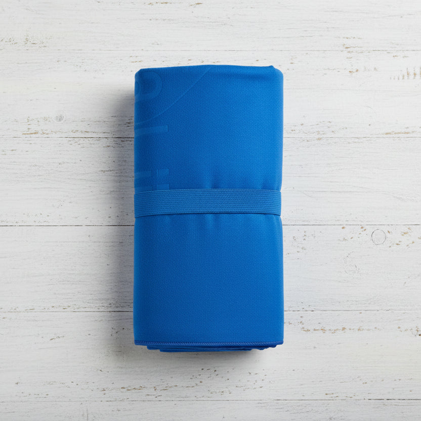 A royal blue Talii Towel draped over a flat surface with a person standing in front, holding the towel at the top, showing the size and colour of the towel.