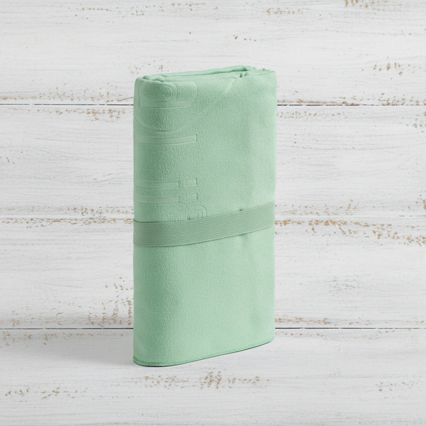 A sea foam green Talii Towel draped over a flat surface with a person standing in front, holding the towel at the top, showing the size and colour of the towel.